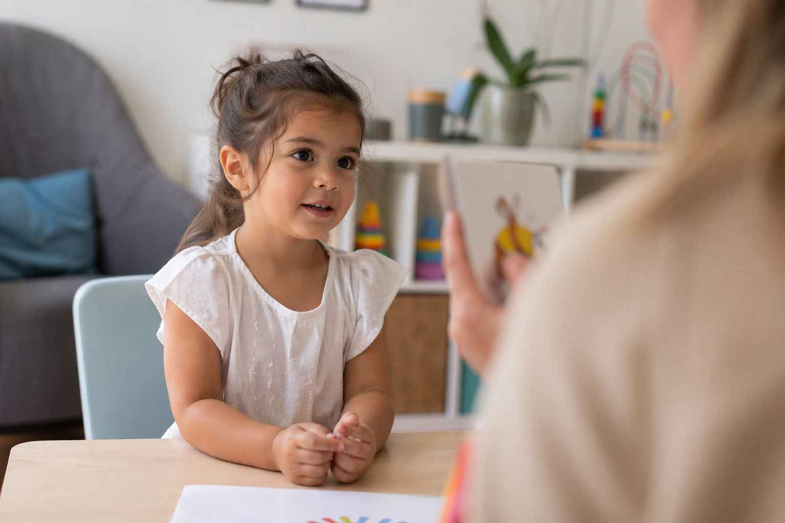A young girl talking with her speech pathologist at a table during a session